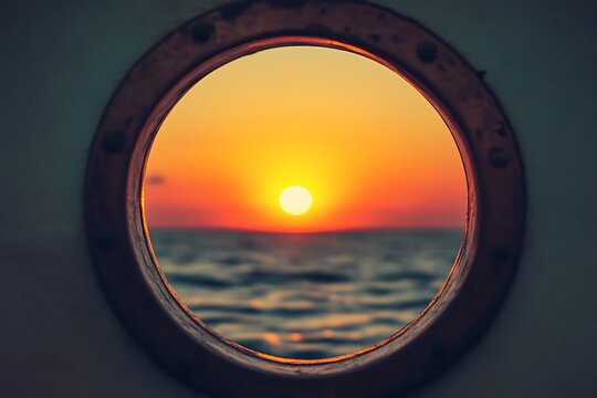 Fototapeta Golden sunset over ocean seen through ship porthole window