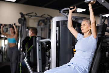 Older sportswoman training at overhead press machine in gym