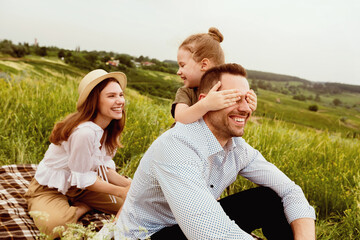 Happy Together. Playful young girl closing her dad's eyes at park, surprising him outside, looking...