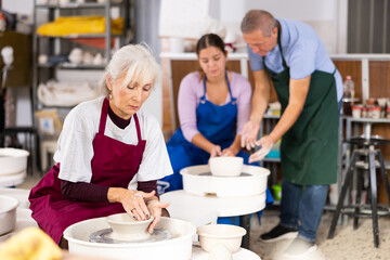 Mature woman learning how to create pottery on potter wheel in a workshop
