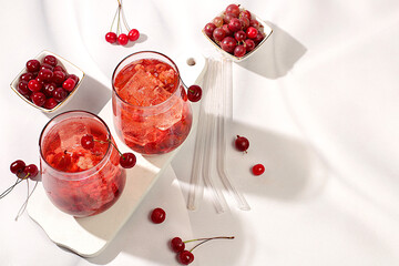 Cold homemade lemonade cocktail, mojito with mint, cherry and gooseberry on a sunny table,...