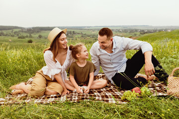 Loving family with adorable child spending weekend together on picnic in the meadow, looking at...