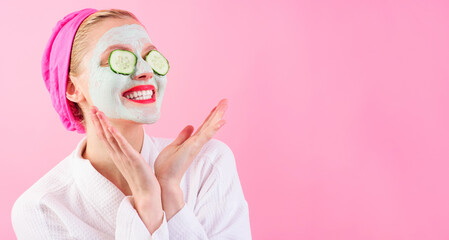 Happy woman with clay cosmetic face mask and fresh cucumber slices on eyes. Beauty, skincare and...