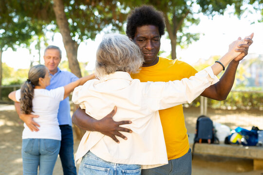 Group of cheerful multiracial adult people of different age enjoying dancing in pairs outdoor at park