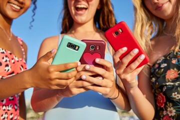 Fototapeta premium Friends using mobile phones standing together on sunny day.