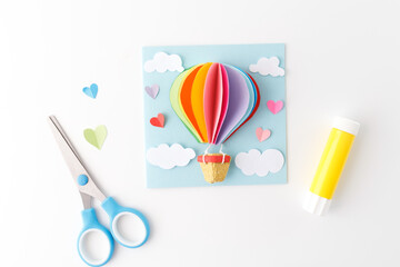 paper craft project hot air balloon. Colorful handmade design with scissors and glue on a blue...