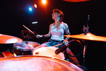 Female drummer performing energetically on stage with colorful lighting