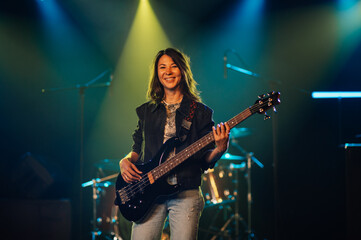 Fototapeta premium Female musician playing bass guitar on stage during concert
