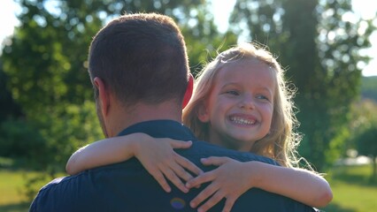 Close up of little girl laughing hugging her dad in park. Family concept. Rear of male parent...