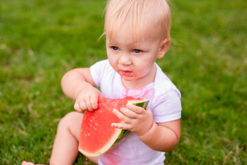 Messy baby eating juicy watermelon with stained shirt on summer day