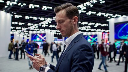 Businessman engaging with smartphone at tech conference amidst crowds