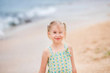 Blonde girl standing on the beach and looking at the camera with the sea in the background on a cloudy summer day