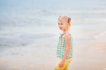 Blonde girl standing on the beach and looking at the camera with the sea in the background on a cloudy summer day