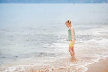 Blonde girl standing on the beach and looking at the camera with the sea in the background on a cloudy summer day