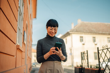 Smiling asian businesswoman using smartphone while walking in the city