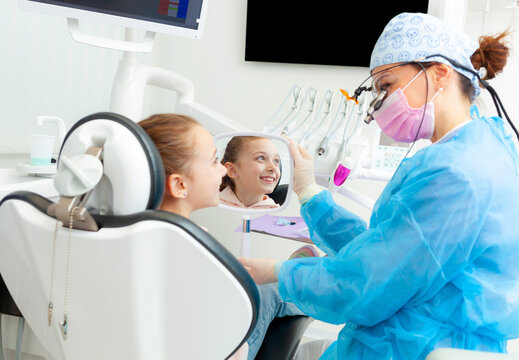 Pediatric dentist showing mirror to smiling girl in dental clinic