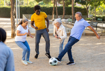 Cheerful males and females kicking the ball in summer park
