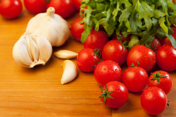 Tomatoes, garlic and rucola on wooden table, focus on foreground