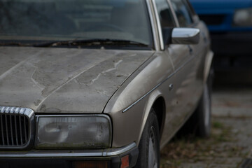 A weathered car that is covered in dust is sitting in a parking lot setting, waiting for its owner