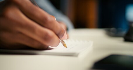 Black freelancer researching online data and writing notes for articles, sitting at his personal...
