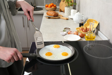 Woman cooking eggs in frying pan on cooktop indoors, closeup
