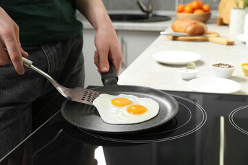 Man taking fried eggs from frying pan in kitchen, closeup