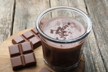 Tasty chocolate milk with shavings and pieces on wooden table, closeup