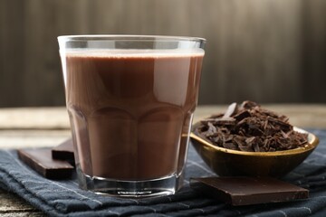 Tasty chocolate milk with shavings and pieces on wooden table, closeup