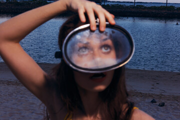Young woman holding a vintage diving mask while gazing upwards by the water