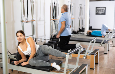 Fototapeta premium Focused young female in sportswear training abs core while lying on side and using Pilates bed in gym