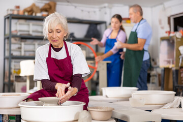 lady on potter's wheel forms vase out of wet clay