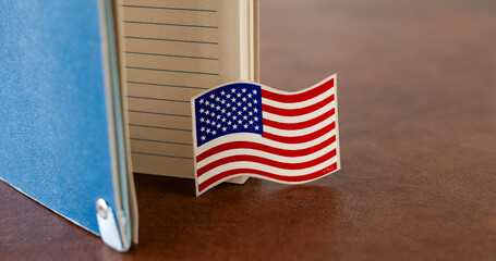 Small USA flag represented as stickers placed near a notebook on a wooden surface, symbolizing travel and politics