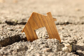 Wooden house model in cracked asphalt demonstrating earthquake disaster