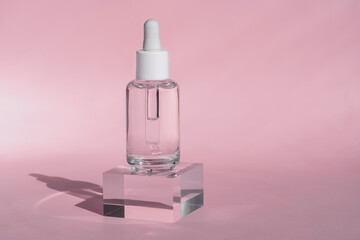 Transparent serum glass dropper bottle with white cap stands on clear acrylic block, set against soft pink background, clean and minimalistic beauty product design