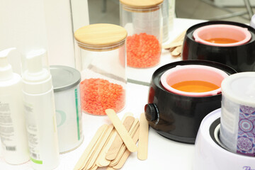 Hot depilatory wax in heater, spatulas and other products on white table