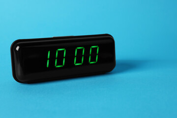 Digital alarm clock showing 10:00 o'clock on light blue background