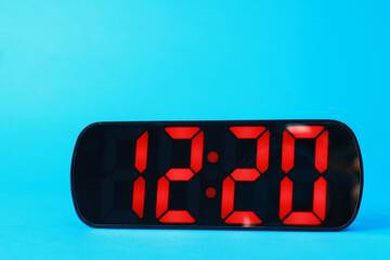 Digital alarm clock showing 12:20 o'clock on light blue background, closeup
