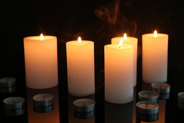 Many burning candles on mirror surface against black background, closeup