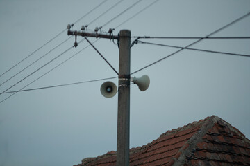 Power pole featuring loudspeakers against a cloudy background, showing telecommunications...