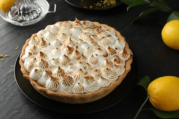 Delicious meringue pie and lemons on black textured table, closeup