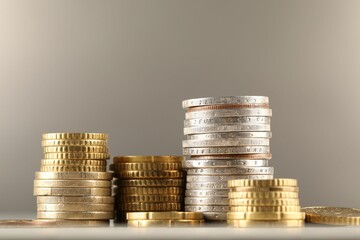 Stacks of different coins on light table against grey background, closeup