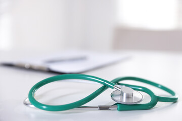 Stethoscope and paperwork on white desk in hospital, selective focus. Space for text