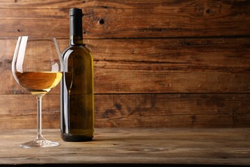 Tasty white wine in glass and bottle on wooden table, space for text