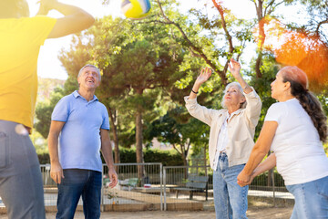 Joyful middle aged mixed-race people having good time together while playing volleyball in public...