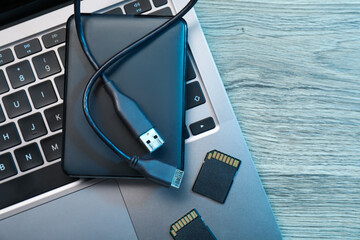 Hard disk drive with USB cable, SD memory cards and laptop on wooden table, top view. Space for text