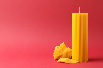 Beautiful beeswax candle and pieces of wax on red background, space for text