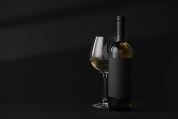 Bottle of wine and wineglass on black background, space for text