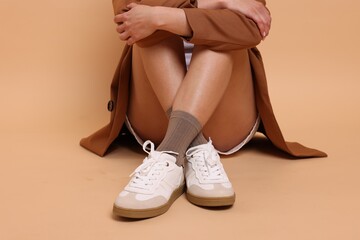 Woman in stylish brown socks and sneakers on beige background, closeup