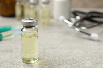 Hepatitis vaccine in glass vial and stethoscope on grey table, closeup. Space for text