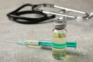 Hepatitis vaccine in glass vial, syringe and stethoscope on grey table, closeup